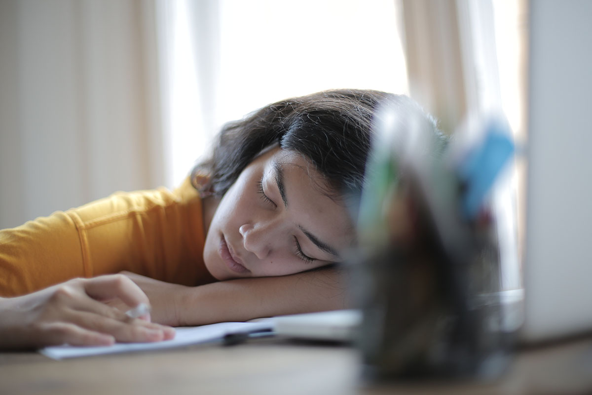 Woman asleep with pen in hand laying head on notebook